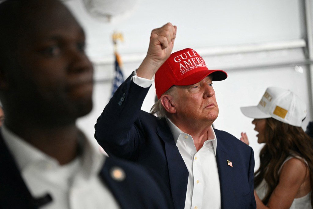 Donald Trump raising his fist while wearing a red "Gulf America" hat.